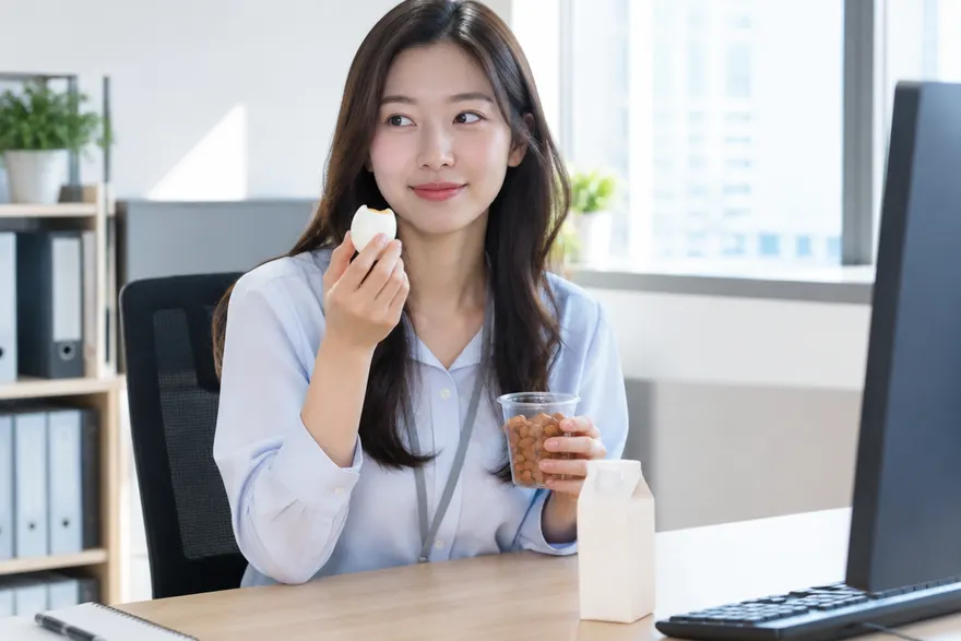 한국인 직장인이 사무실 책상에서 삶은 달걀과 두유, 견과류를 간식으로 먹는 모습